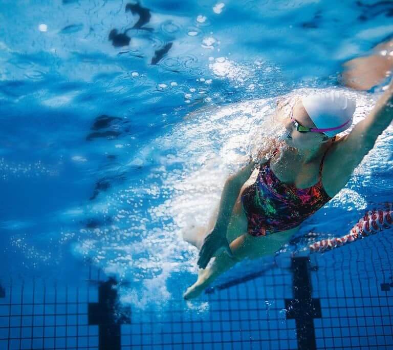 Young girl in goggle and swimming cap doing underwater swimming strokes